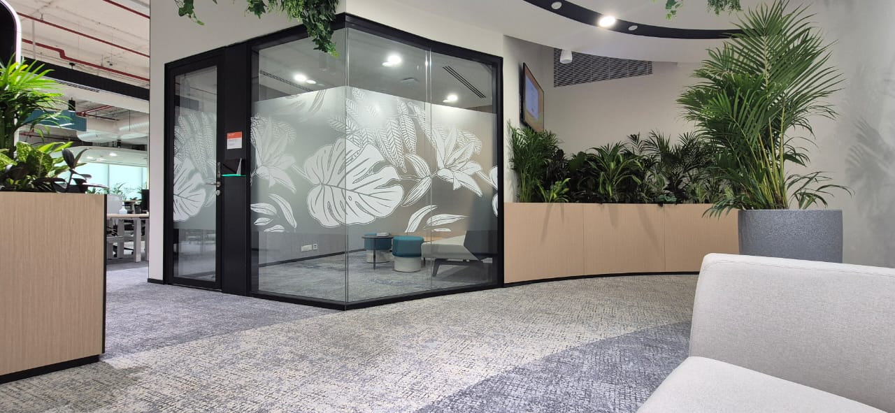 Glass meeting pod with botanical leaf decals beside a curved planted bench, delivered by Ananya Interiors in Bengaluru
