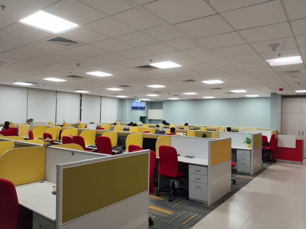 Open-plan workstations with mustard privacy screens and red task chairs in the Home Credit office, Bengaluru