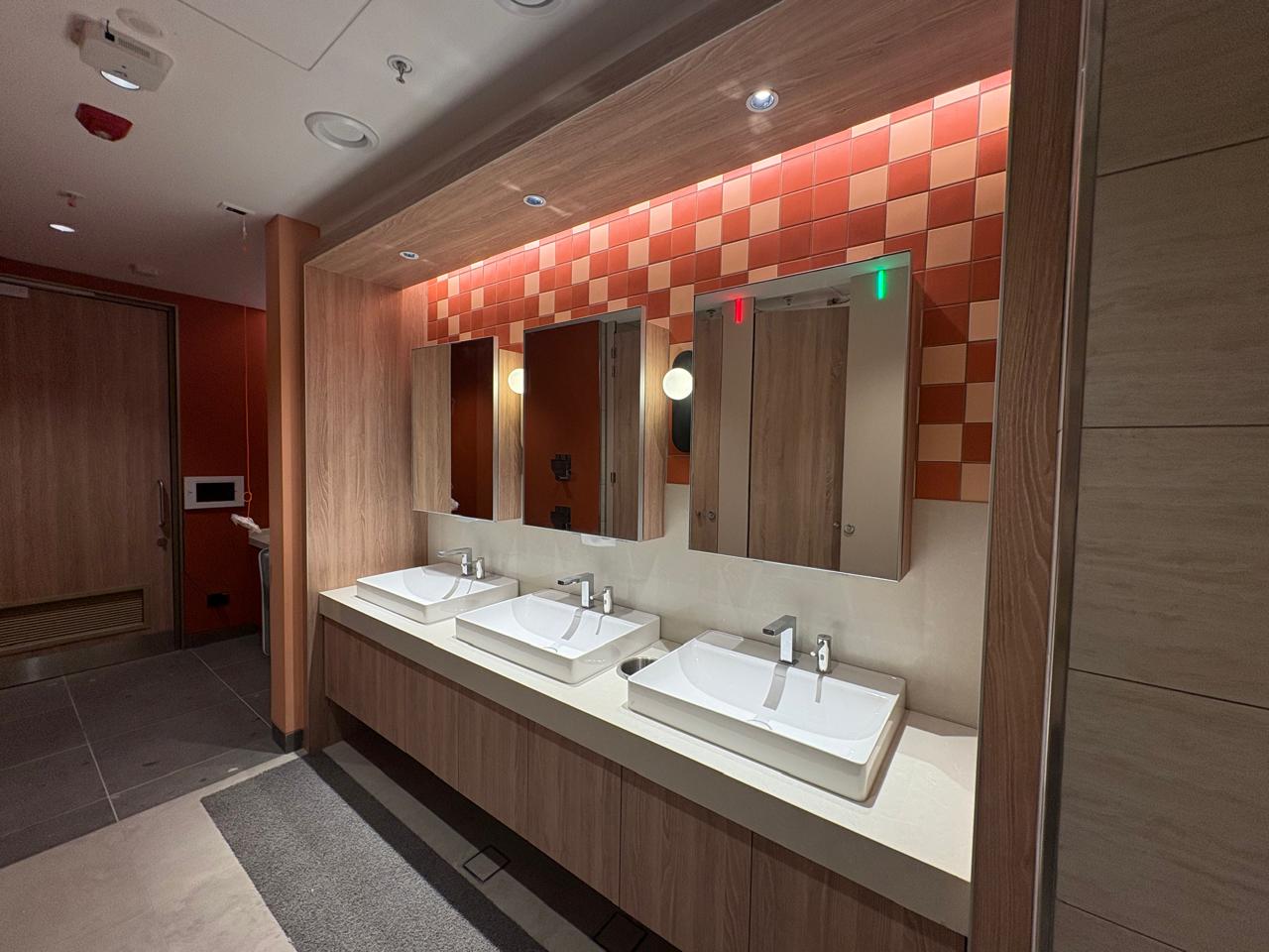 Washroom vanity run with warm wood panelling and checkerboard tiles at the Intuit Bengaluru product development centre