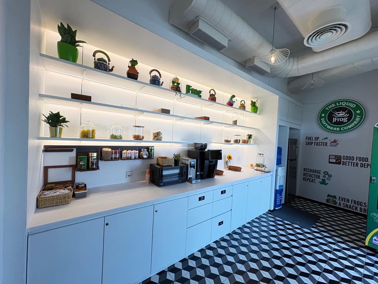 JFrog India office tea point with backlit shelves, coffee station and the 'Fuel up. Ship faster.' brand wall, Bengaluru