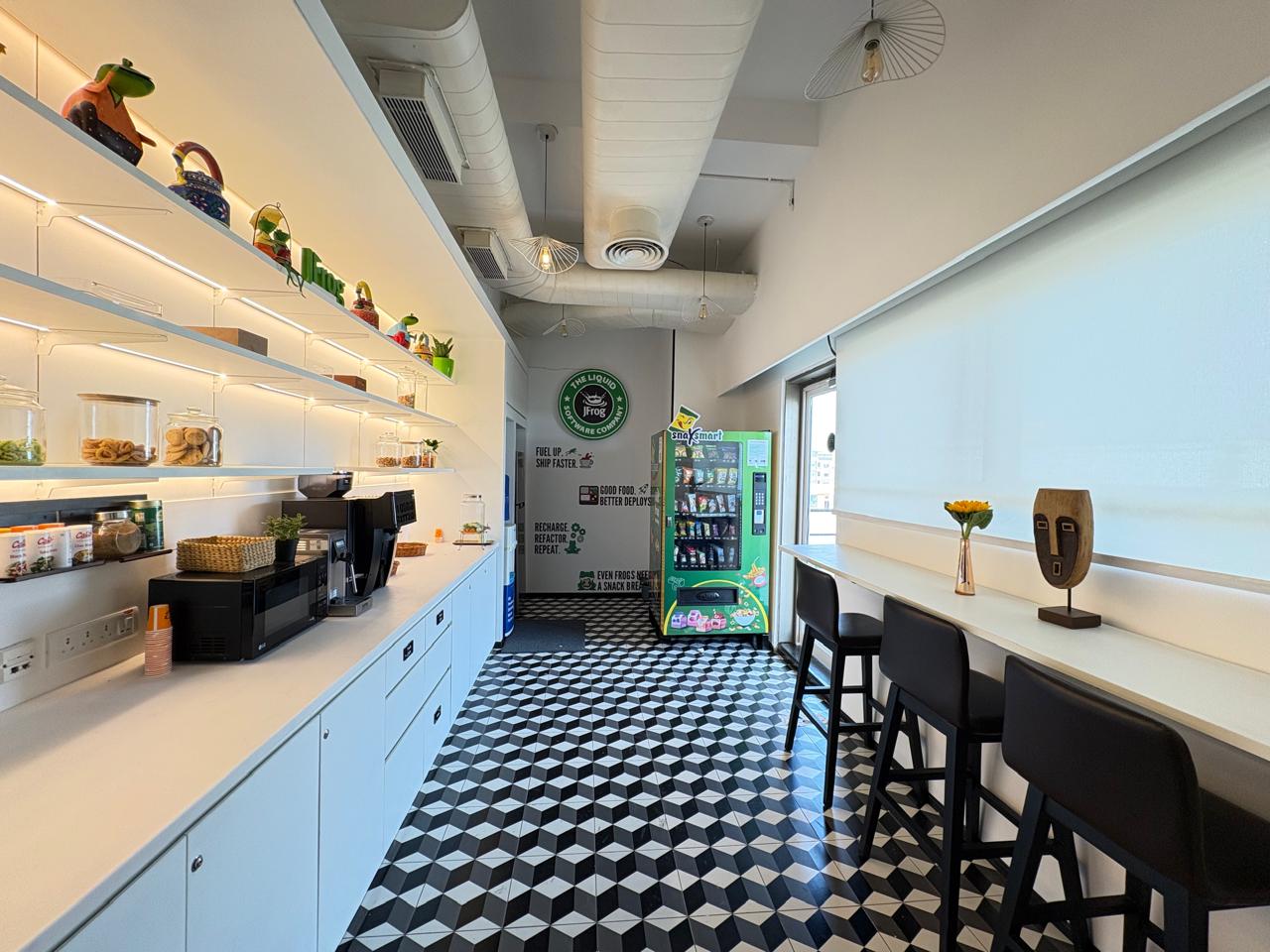 JFrog India office tea point with glass snack jars and the JFrog brand sign beside the vending machine, delivered by Ananya Interiors in Bengaluru