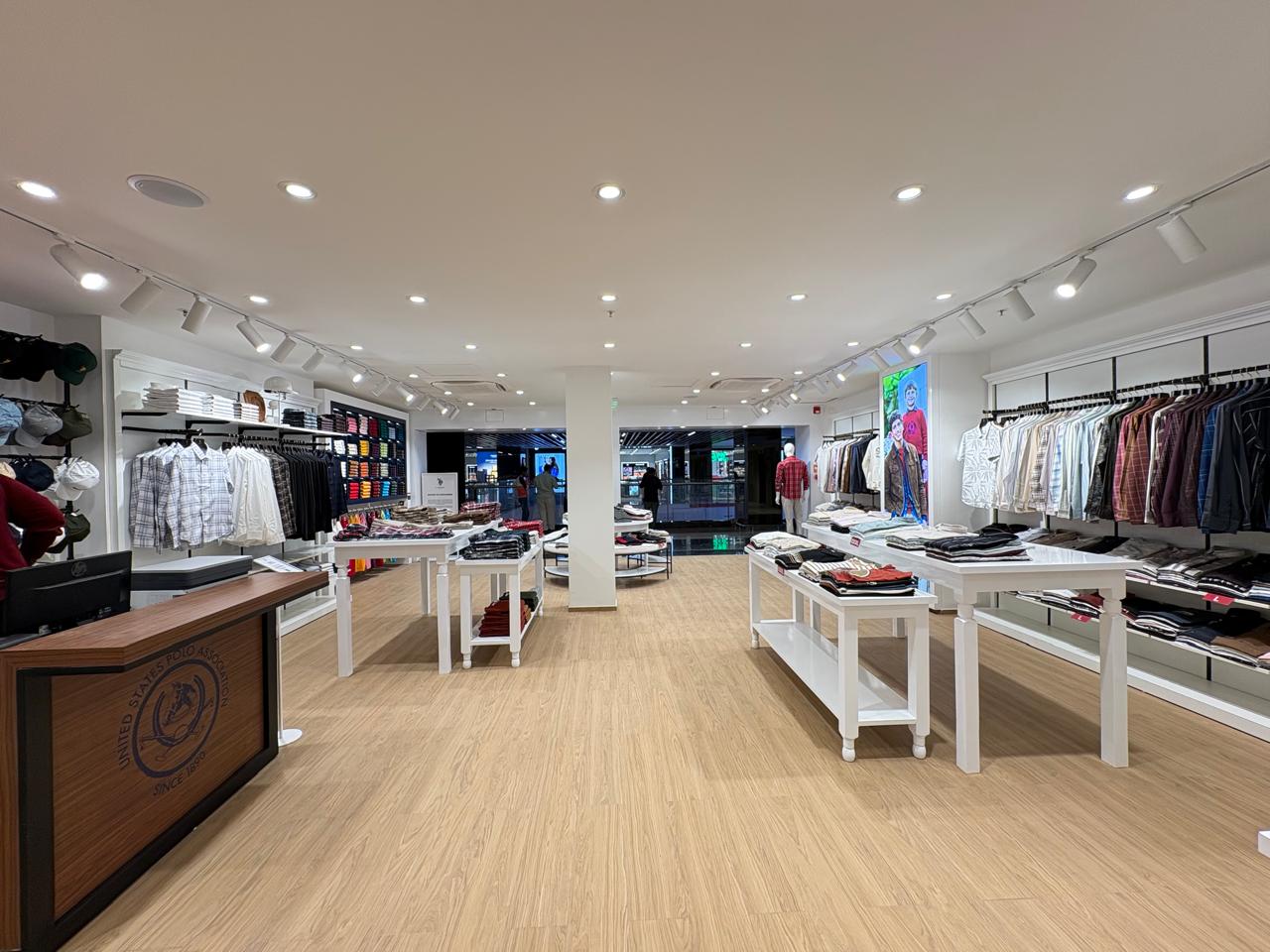 Bright shop floor of the U.S. Polo Assn. mall store with central column and backlit campaign lightbox, Bengaluru